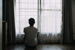 person sitting in front of window wonders about the connection between isolation and depression